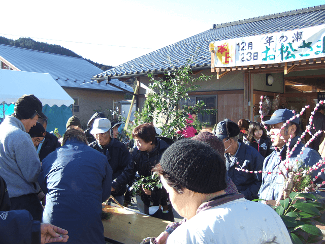 写真5：1年間の感謝の意を込めた村のイベントであるお松さま祭りの様子を表す写真。組合が協力し、門松やしめ飾りなど迎春用品の販売のほか、体を温める数種類の大鍋や特産品が販売される。