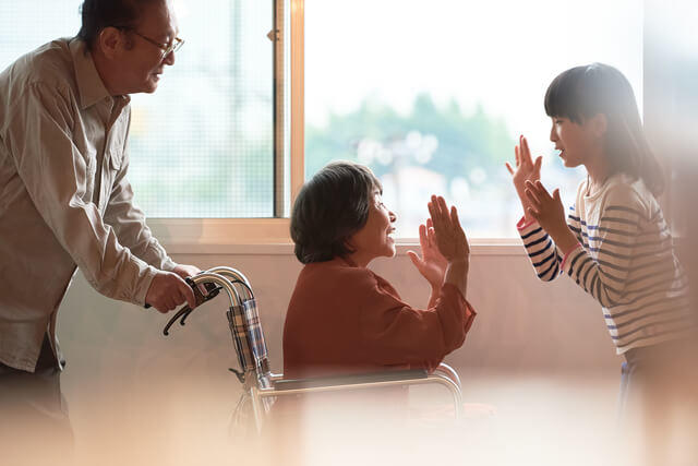 世代間の交流を表す施設で暮らすお婆さんと訪問する孫が笑いあう様子を表す写真。